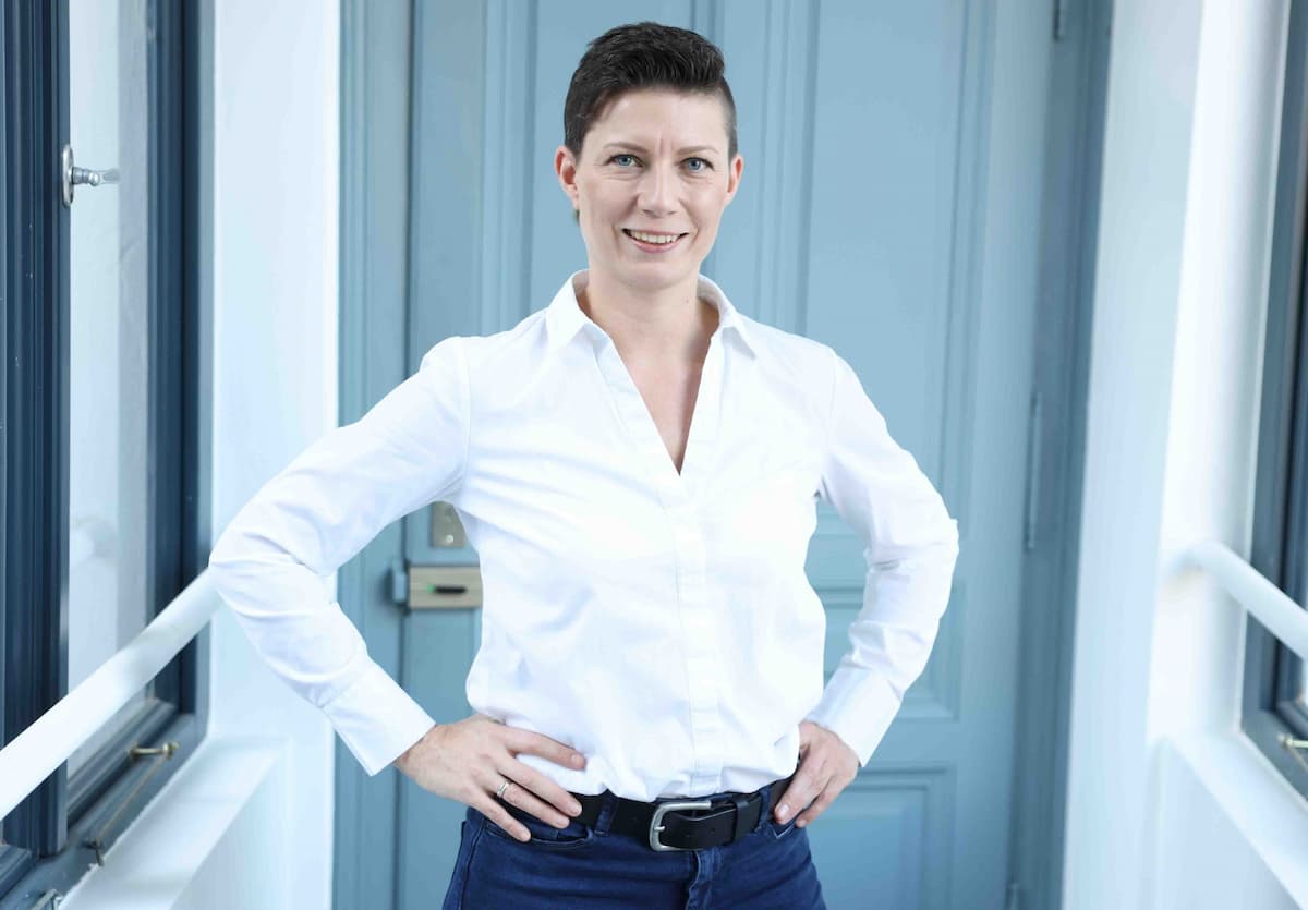 Portrait von Angelique Sturmlechner in weißem Hemd vor blauem Hintergrund. PR Beauftragte von Permedio.